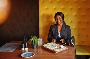 African american businesswoman eating cheese pizza in cafe. Black girl having rest. photo