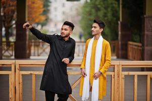 Two indian stylish mans friends in traditional clothes posed outdoor and making selfie on phone. photo