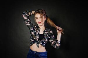 Handsome brunette girl wear military shirt and jeans, posing at studio against gray background. Studio model portrait. photo