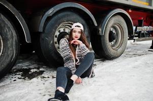 Brunette stylish casual girl in cap sitting against truck wheels. photo