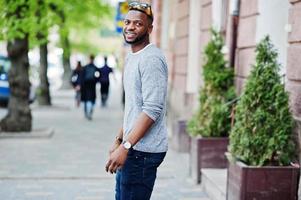 Elegante chico afroamericano con suéter gris y gafas de sol negras posadas en la calle. chico negro de moda. foto