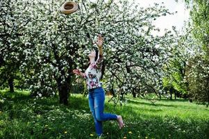 Spring portrait of brunette girl in pink glasses and hat at green blossom garden. photo