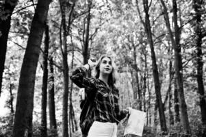 retrato de una joven y hermosa mujer rubia con camisa de tartán sosteniendo un mapa en el bosque. foto