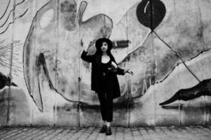 Sensual girl all in black, red lips and hat. Goth dramatic woman hold white chrysanthemum flower against graffiti wall. Black and white portrait. photo