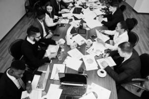 Multiracial business team addressing meeting around boardroom table, working together and write something on papers. photo