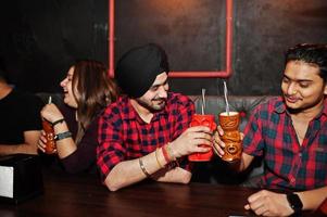 Group of indian friends having fun and rest at night club, drinking cocktails. photo