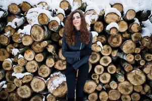 Elegance curly girl in leather jacket at snowy forest park at winter against stumps. photo