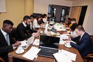 Multiracial business team addressing meeting around boardroom table, working together and write something on papers. photo