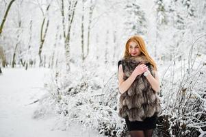 Red haired girl in fur coat walking at winter snowy park. photo
