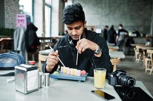 Casual and stylish young asian man with earphones at cafe eating sushi. photo