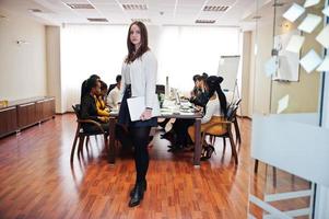 Face of handsome european business woman, holding laptop on the background of business peoples multiracial team meeting, sitting in office table. photo
