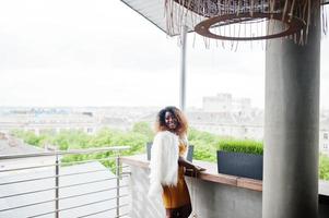 Glamour african american woman in yellow dress and white woolen cape with handbag posed at balcony. photo