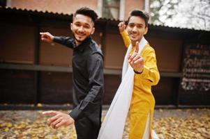 Two indian stylish mans friends in traditional clothes dancing outdoor. Navaratri dance. photo