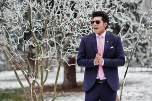 elegante modelo de hombre macho indio con traje y corbata rosa, gafas de sol posadas en el día de invierno. foto
