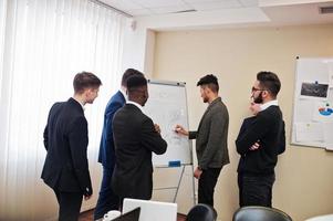 los colegas masculinos que trabajan en equipo cooperan, el equipo multirracial de empleados se concentra en la planificación de proyectos contra rotafolios y discute ideas. foto