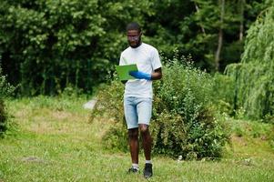 hombre voluntario africano con portapapeles en el parque. Concepto de voluntariado, caridad, personas y ecología de África. foto