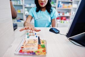 farmacéutico afroamericano que trabaja en la farmacia del hospital. salud africana. cajero con dinero en euros. foto