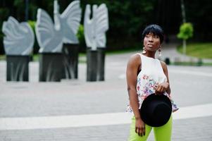 increíble mujer modelo afroamericana en pantalones verdes y sombrero negro posó en el parque. foto