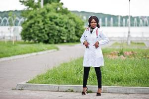 Young african american female doctor in white coat with a stethoscope posed outdoor. photo