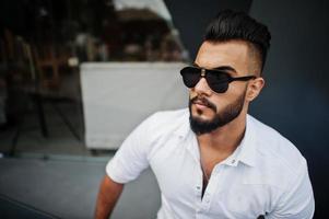 Close up photo of stylish arabian man model in white shirt and sunglasses. Beard attractive arab guy.