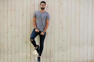 Handsome tall arabian beard man model at stripped shirt posed outdoor against wooden background. Fashionable arab guy. photo