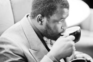 Stylish African American man model in gray jacket tie drink coffee at cafe. Black and white photo. photo