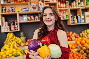 Girl in red holding different vegetables on fruits store. photo