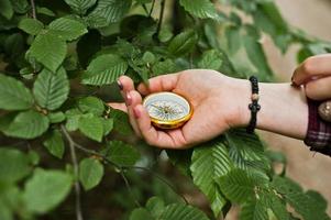 Close-up photo of female hands with compass next to a tree branch.