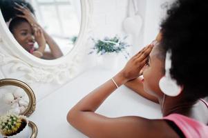 Young african american woman looking at the mirror and listen music on earphones. photo