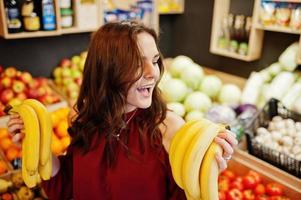 Girl in red holding bananas on fruits store. photo