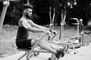 African american male athlete sport man with running sports arm case for mobile phone, doing exercises on the street workout simulators. photo