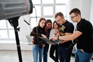 fotógrafo explicando sobre la toma a su equipo en el estudio y mirando en la computadora portátil. hablando con sus asistentes sosteniendo una cámara durante una sesión de fotos. trabajo en equipo y lluvia de ideas. foto