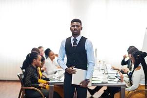 Face of handsome african business man, holding laptop on the background of business peoples multiracial team meeting, sitting in office table. photo