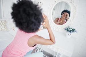 Young african american woman looking at the mirror and listen music on earphones. photo