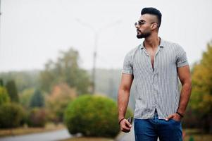 Fashionable tall arab beard man wear on shirt, jeans and sunglasses posed on park and hold wallet at hand. photo