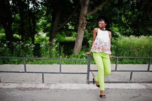 increíble mujer modelo afroamericana en pantalones verdes y sombrero negro posó en el parque. foto