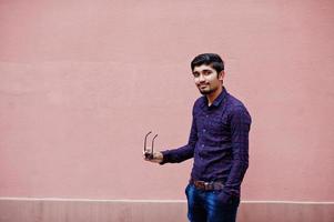 Young indian man on shirt and sunglasses posed against pink wall. photo