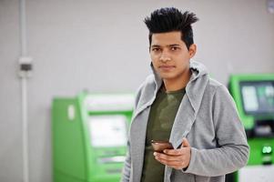 Young stylish asian man with mobile phone against row of green ATM. photo