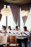 Happy african friends sitting, chatting in cafe and eat food. Group of black peoples meeting in restaurant and have dinner. photo