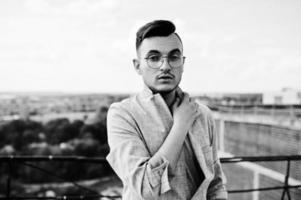 Dreamer stylish macho man in gray suit and glasses posed on the roof. photo