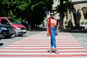 Stylish african american woman walking on crosswalk or pedestrian crossing with mobile phone at hand. photo