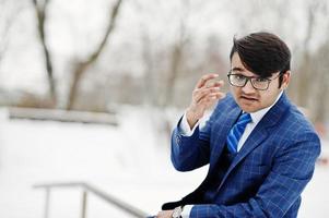 elegante hombre de negocios indio con traje y gafas posado en el día de invierno al aire libre. foto