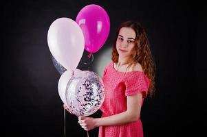 Young girl in red dress with balloons against black background on studio. photo