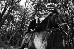 Mystical girl in wreath wear in black at horse in wood. photo