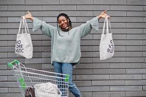 No more plastic. African woman with shopping cart trolley and eco bags posed outdoor market. photo