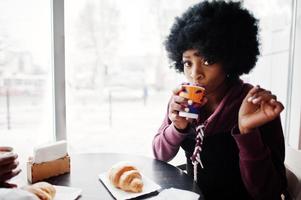 Curly hair african american woman wear on sweater posed at cafe indoor with cup of tea or coffee. photo
