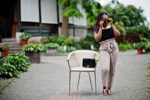 Stylish african american woman in sunglasses posed outdoor at chair. photo