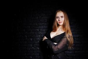 Studio shot of brunette girl in black blouse with bra and shorts against black brick wall. photo