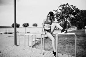 Sexy curly model girl in red top, jeans denim shorts, cup sunglasses and sneakers posed against steel rails. photo