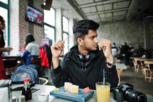 Casual and stylish young asian man with earphones at cafe eating sushi. photo